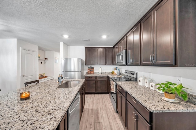 kitchen with dark brown cabinets, sink, stainless steel appliances, and light wood-type flooring