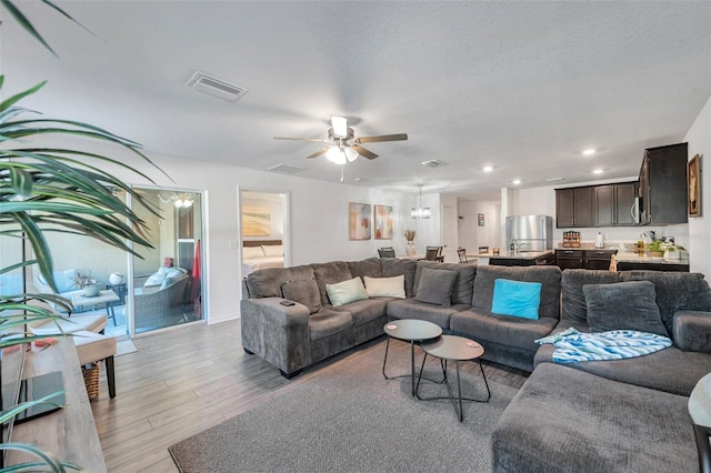 living room with ceiling fan, light wood-type flooring, and a textured ceiling