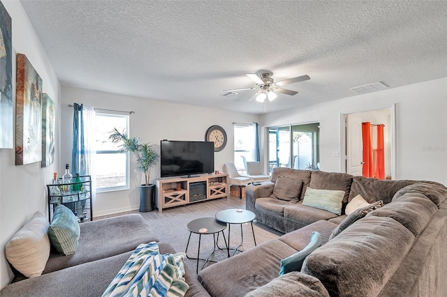 living room with ceiling fan, a textured ceiling, a wealth of natural light, and light hardwood / wood-style flooring