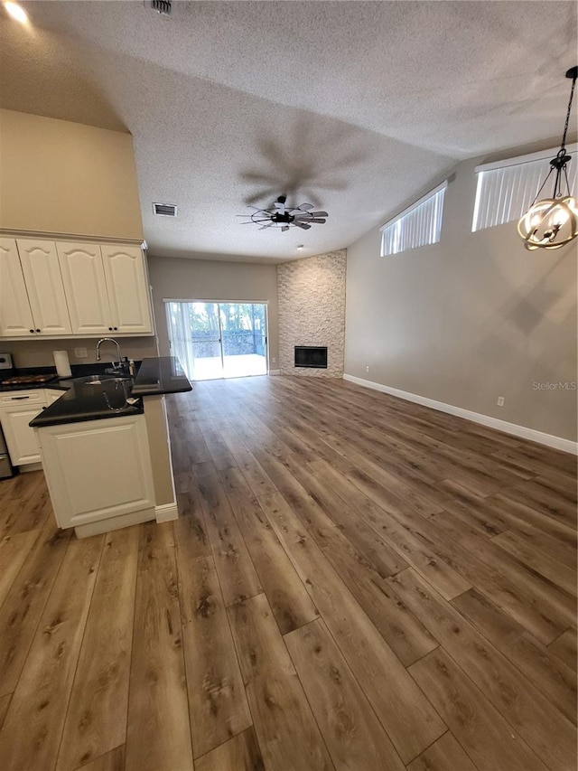 kitchen with white cabinets, dark countertops, open floor plan, hanging light fixtures, and ceiling fan with notable chandelier