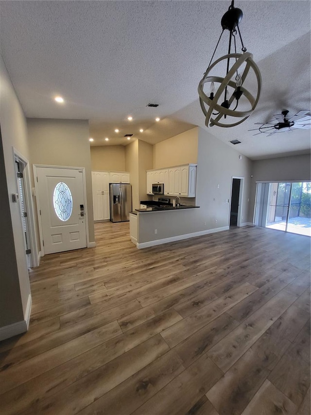 unfurnished living room with lofted ceiling, ceiling fan, a textured ceiling, wood finished floors, and baseboards