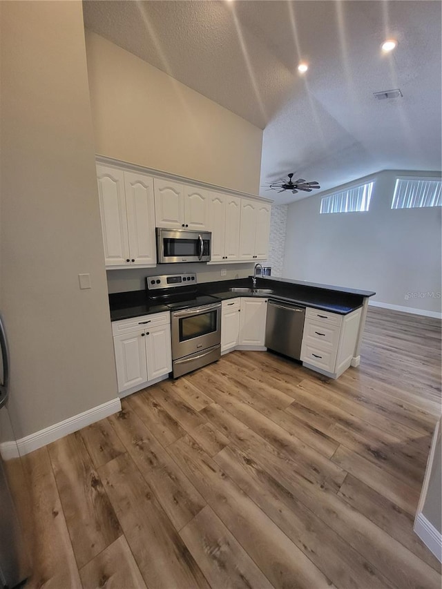 kitchen featuring stainless steel appliances, dark countertops, a peninsula, and white cabinets