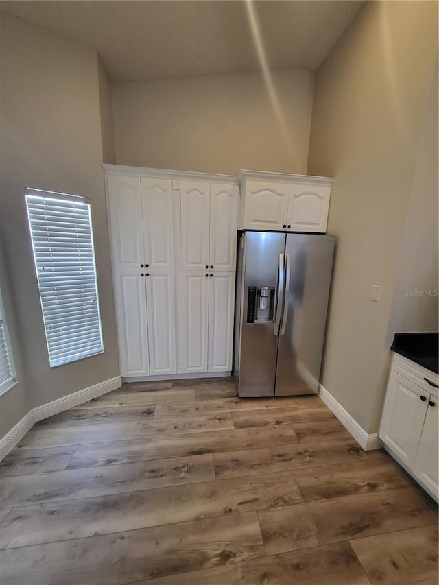 kitchen featuring light wood finished floors, baseboards, stainless steel fridge with ice dispenser, dark countertops, and white cabinetry