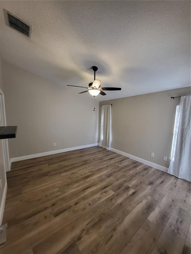 unfurnished living room featuring baseboards, visible vents, a ceiling fan, dark wood finished floors, and a textured ceiling