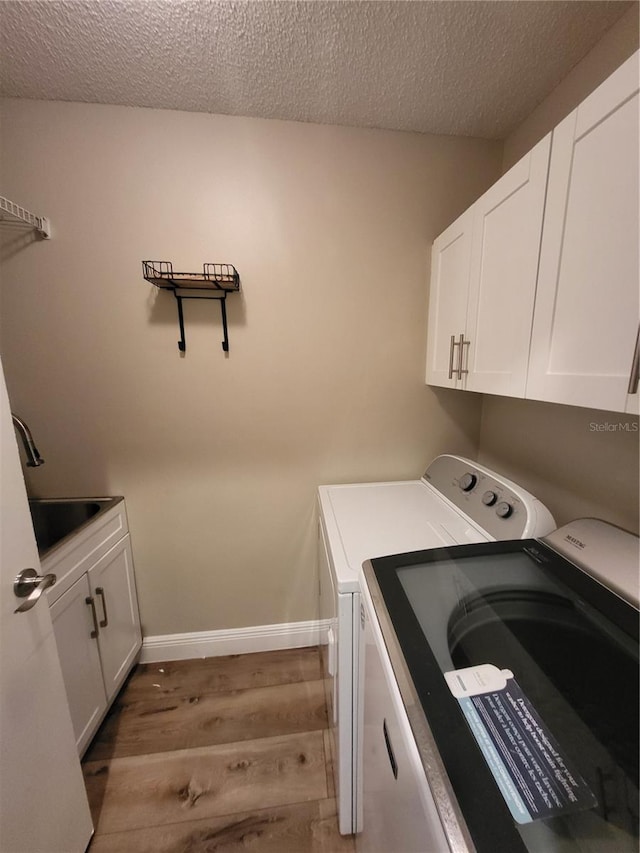 laundry area with a textured ceiling, a sink, cabinet space, light wood finished floors, and washer and clothes dryer