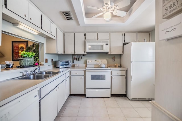 kitchen with white appliances, a sink, white cabinetry, light countertops, and a tray ceiling