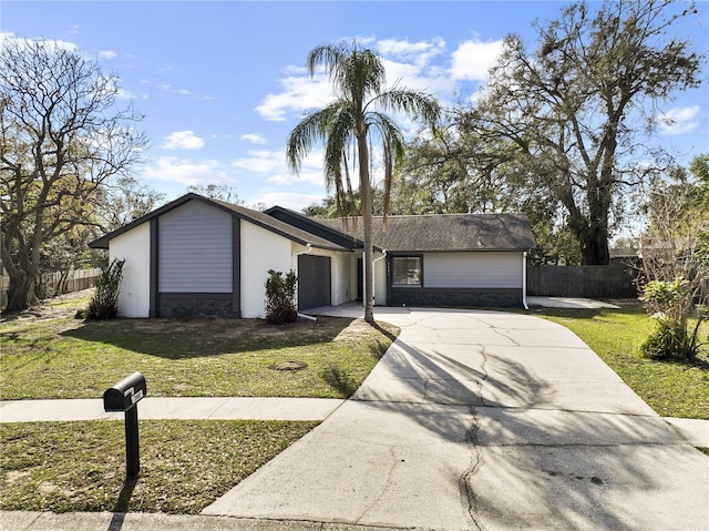 mid-century home with a garage, driveway, stone siding, fence, and a front lawn