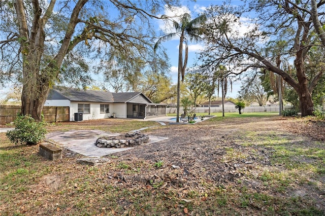 view of yard featuring a patio, an outdoor fire pit, a sunroom, central AC, and fence