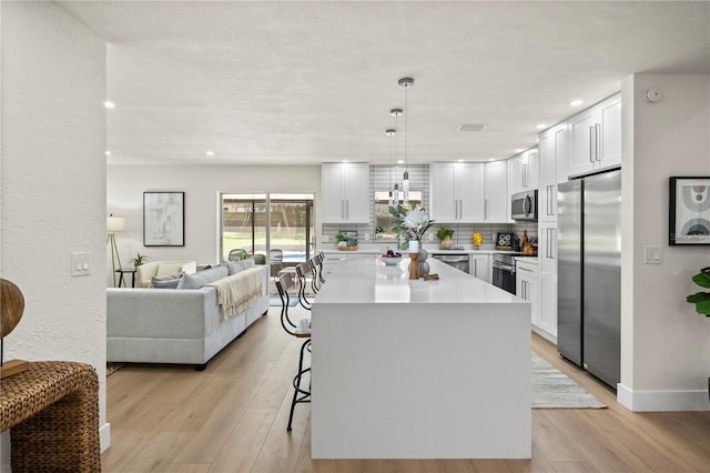 kitchen with a breakfast bar, light wood finished floors, tasteful backsplash, appliances with stainless steel finishes, and white cabinets