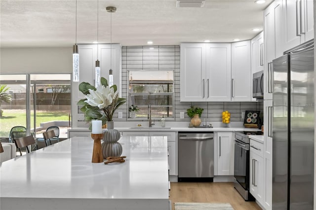 kitchen featuring light wood-style flooring, stainless steel appliances, a sink, light countertops, and backsplash