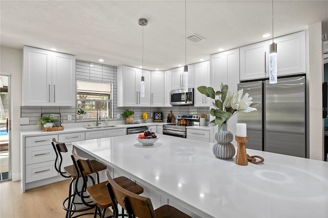 kitchen featuring stainless steel appliances, a sink, visible vents, light countertops, and decorative backsplash