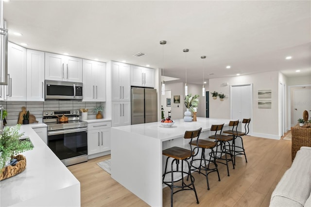 kitchen with stainless steel appliances, light wood finished floors, a breakfast bar area, and tasteful backsplash