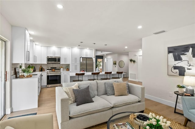 living area featuring baseboards, light wood finished floors, visible vents, and recessed lighting