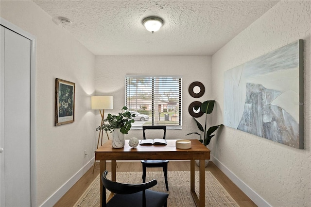 office space featuring baseboards, wood finished floors, and a textured wall