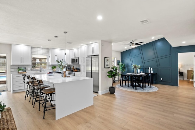 kitchen featuring visible vents, stainless steel appliances, a kitchen bar, a decorative wall, and backsplash