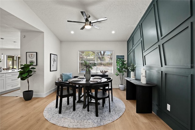 dining area featuring a textured ceiling, ceiling fan, a decorative wall, baseboards, and light wood-style floors