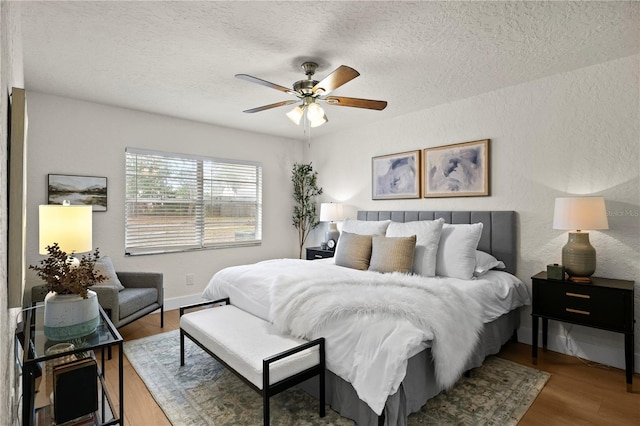 bedroom with a textured ceiling, a textured wall, ceiling fan, and wood finished floors