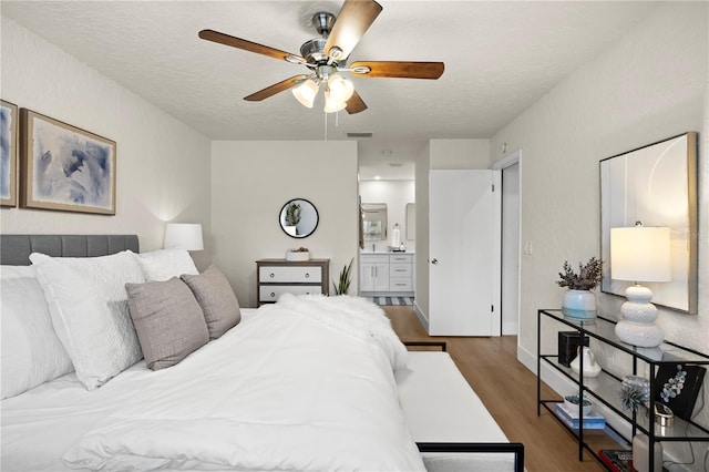 bedroom with visible vents, ceiling fan, a textured ceiling, ensuite bath, and wood finished floors