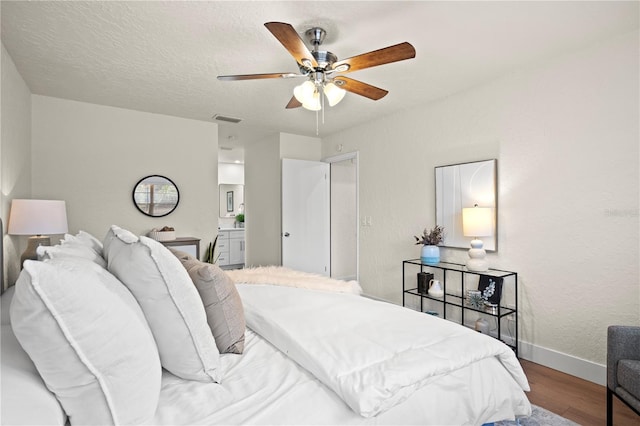 bedroom featuring visible vents, connected bathroom, a textured ceiling, wood finished floors, and baseboards