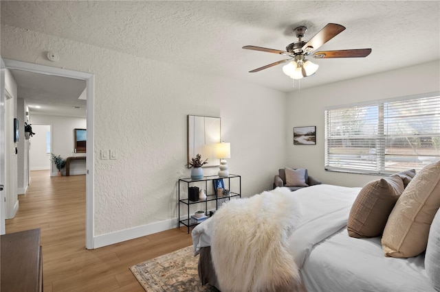 bedroom with baseboards, a textured wall, ceiling fan, a textured ceiling, and light wood-style floors