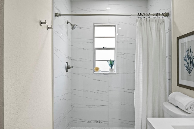 bathroom with a textured wall, a marble finish shower, and toilet