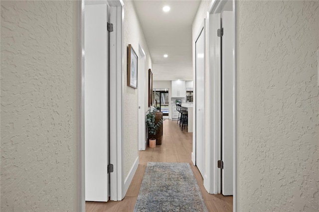 corridor with light wood-type flooring, recessed lighting, and a textured wall