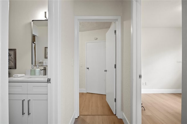 hall featuring light wood finished floors, a sink, and baseboards