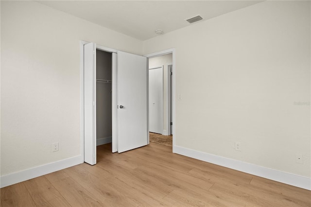 unfurnished bedroom featuring light wood-style flooring, a closet, visible vents, and baseboards