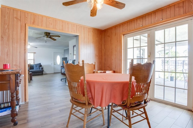 dining room featuring a ceiling fan, light wood-style flooring, and wooden walls