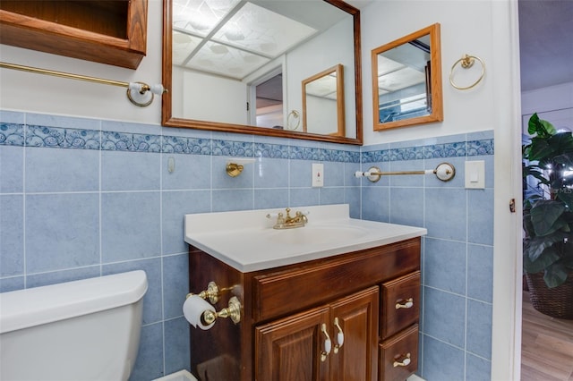 bathroom with tile walls, a wainscoted wall, vanity, and toilet