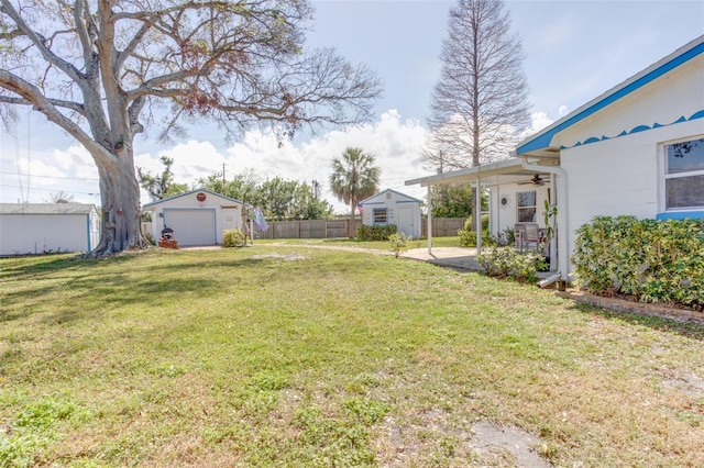 view of yard featuring a detached garage, a storage shed, a ceiling fan, fence, and an outdoor structure