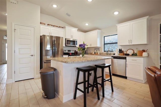 kitchen with a kitchen island, white cabinetry, stainless steel appliances, and vaulted ceiling