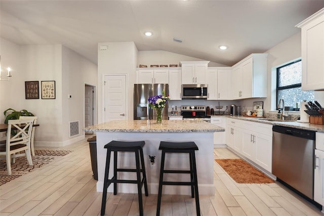 kitchen featuring visible vents, a center island, light stone counters, stainless steel appliances, and a sink