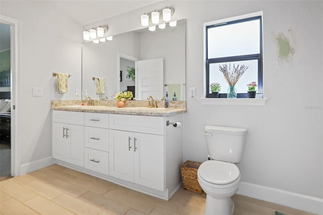 bathroom featuring double vanity, toilet, baseboards, and a sink