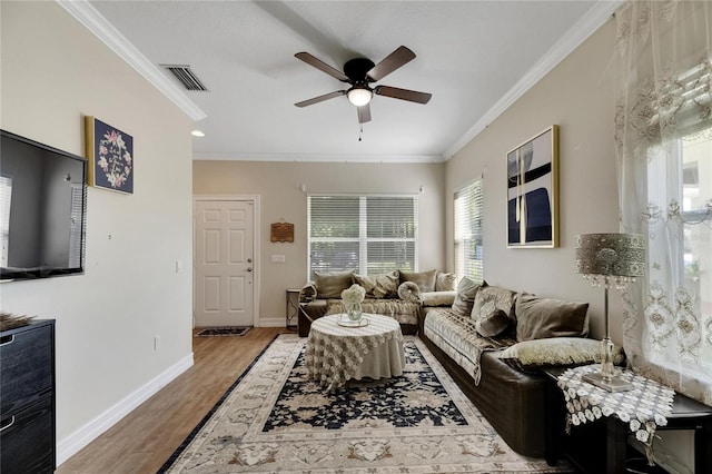 living area with ceiling fan, wood finished floors, visible vents, baseboards, and ornamental molding