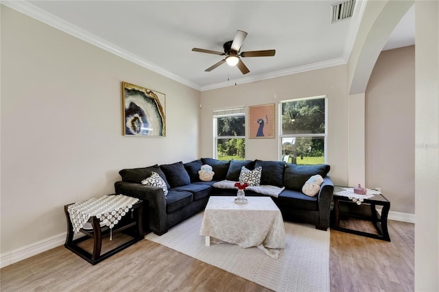 living room featuring arched walkways, crown molding, visible vents, light wood-style flooring, and baseboards