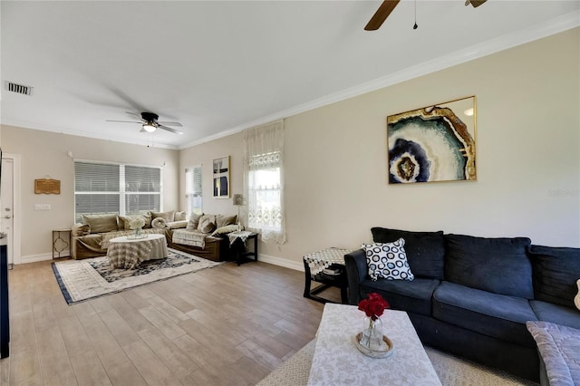 living room with light wood-style flooring, visible vents, baseboards, and ornamental molding