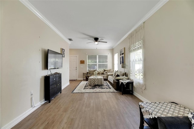 living area featuring visible vents, light wood-style floors, ornamental molding, a ceiling fan, and baseboards