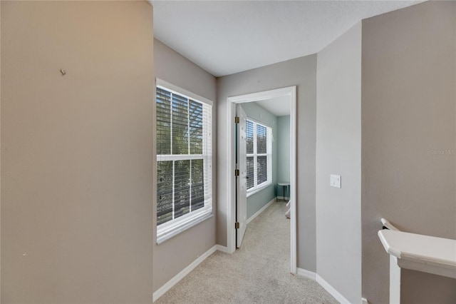 hallway featuring an upstairs landing, baseboards, and light colored carpet