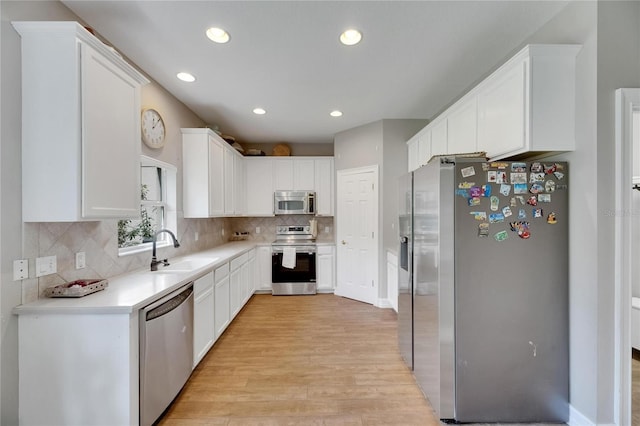 kitchen with stainless steel appliances, a sink, light wood-style floors, white cabinets, and light countertops