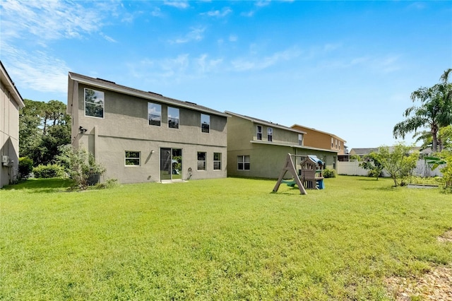 back of house featuring a lawn, a playground, fence, and stucco siding