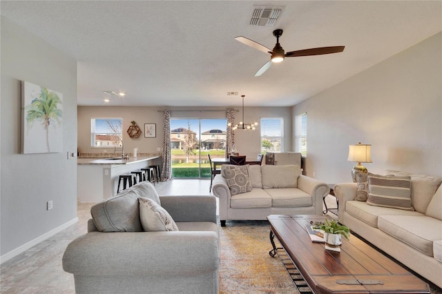 living area featuring baseboards, visible vents, a textured ceiling, and ceiling fan with notable chandelier