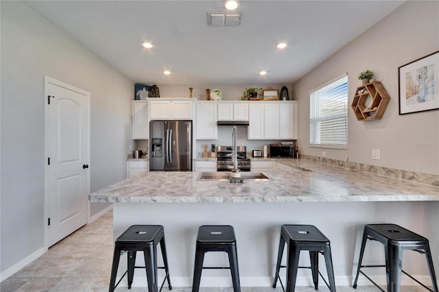 kitchen featuring stainless steel appliances, visible vents, a kitchen breakfast bar, white cabinets, and light countertops