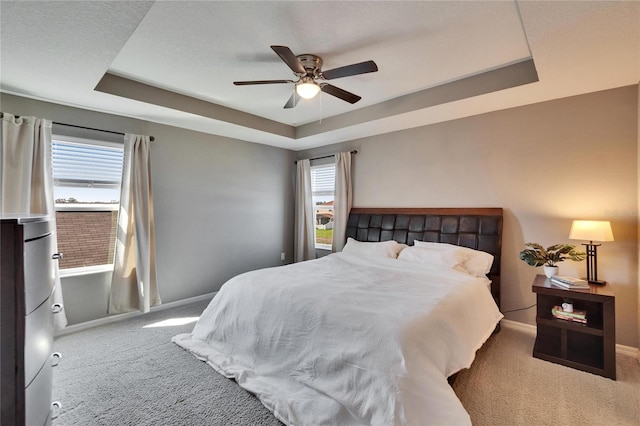 carpeted bedroom with ceiling fan, a tray ceiling, and baseboards