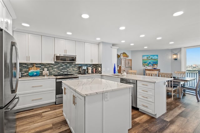 690 Island Way Unit 1003, Clearwater Beach, FL 33767 - kitchen featuring appliances with stainless steel finishes, a peninsula, a sink, decorative backsplash, and dark wood-style floors
