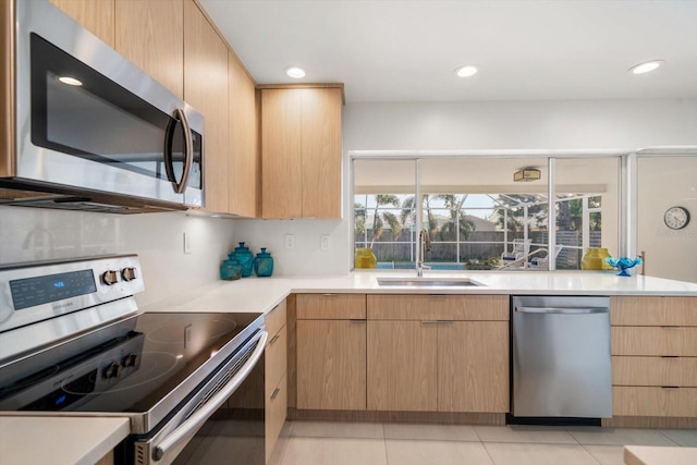 kitchen featuring appliances with stainless steel finishes, light countertops, a sink, and light brown cabinetry