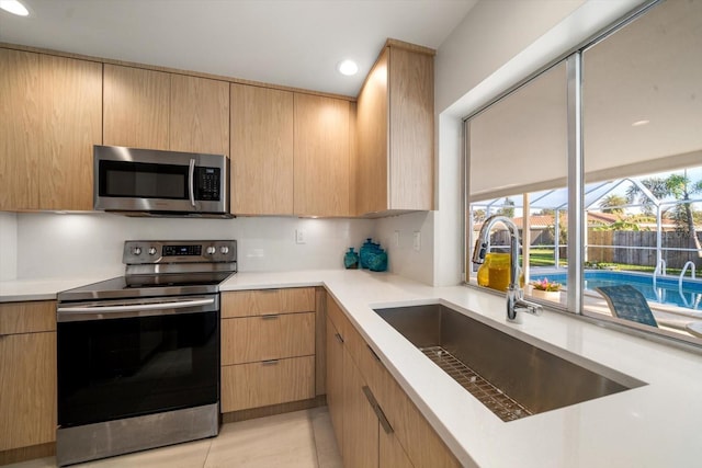 kitchen with a sink, stainless steel appliances, light countertops, and light brown cabinetry