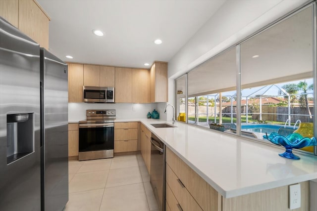 kitchen featuring stainless steel appliances, light countertops, light brown cabinets, and a sink