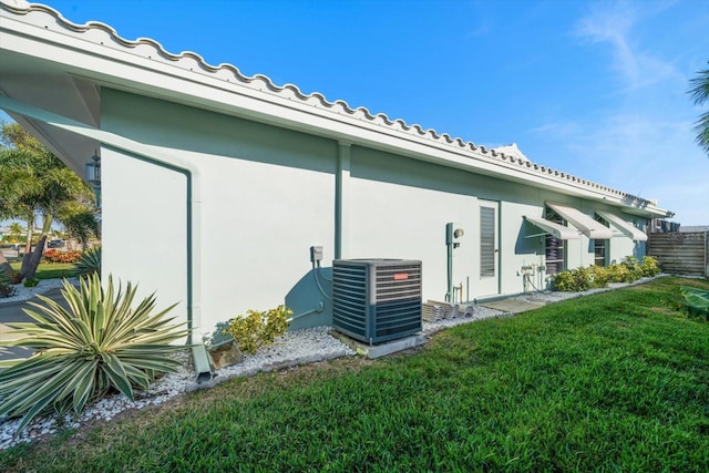 view of side of home with central AC, a lawn, fence, and stucco siding