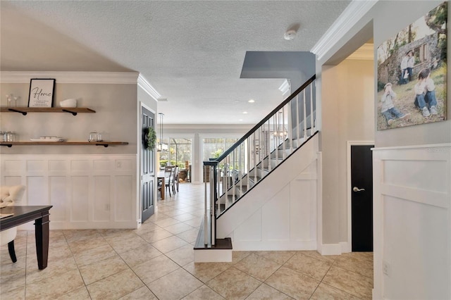 stairway with a textured ceiling, a decorative wall, ornamental molding, wainscoting, and tile patterned floors